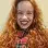 I am a white woman, with long curly red hair, small brown eyes, a wide smile, some wrinkles, a large forehead, an angular face, 1 meter and 65 centimeters tall, wearing a red and green plaid scarf with white stripes.
